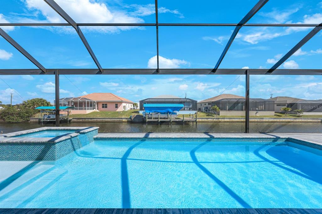 A swimming pool and spa are enclosed by a screen overlooking a canal and houses — 1925 NW 34TH PLACE, CAPE CORAL, FL