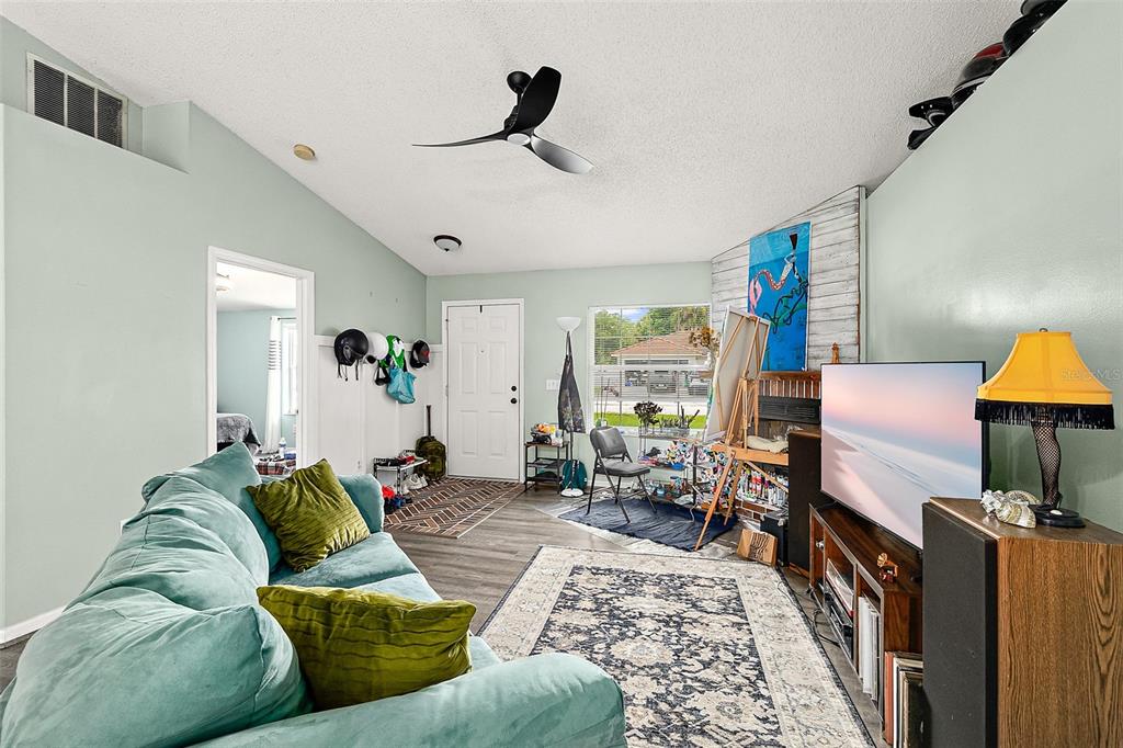 A living room features a teal sofa, a television, an easel, and a ceiling fan — 17 PINELARK LANE, PALM COAST, FL