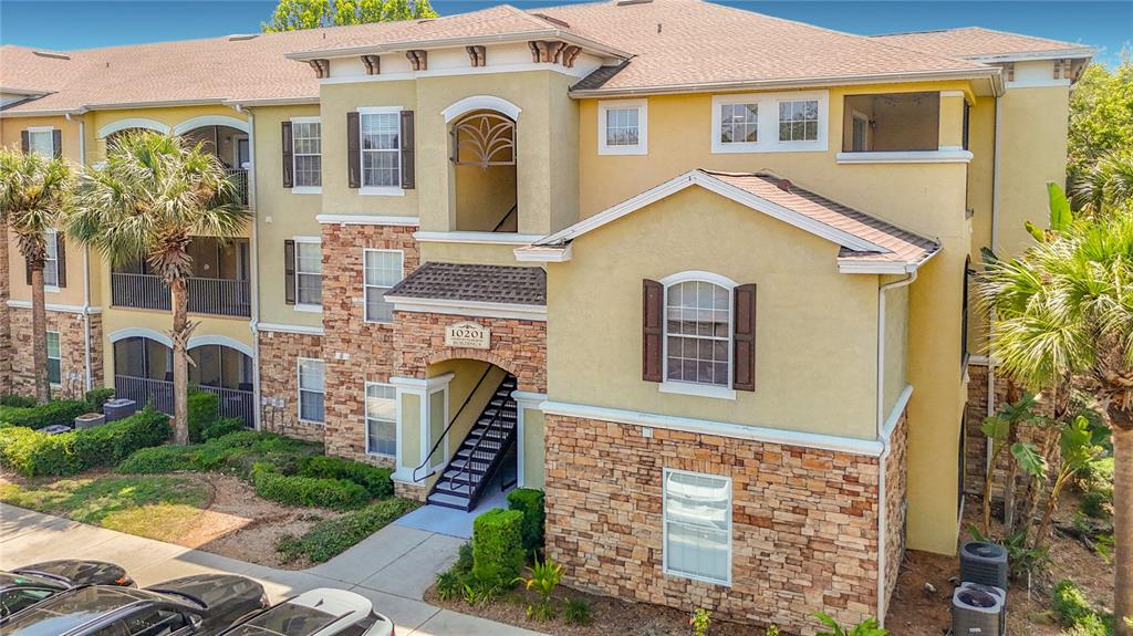 Exterior view of a multi-story apartment building with tan stucco and stone veneer siding — 10201 COURTNEY PALMS BOULEVARD UNIT 203, TAMPA, FL