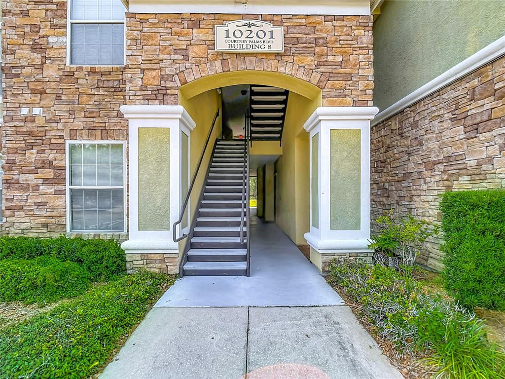 An exterior view of an apartment building entrance featuring stone veneer and a concrete staircase — 10201 COURTNEY PALMS BOULEVARD UNIT 203, TAMPA, FL