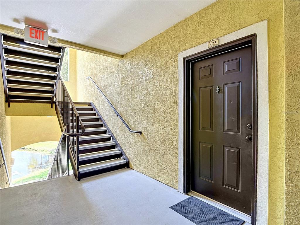 A brown apartment door labeled 203 sits next to an outdoor staircase with metal railings — 10201 COURTNEY PALMS BOULEVARD UNIT 203, TAMPA, FL