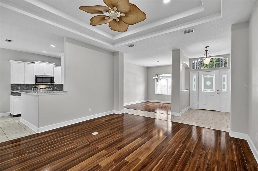 An open-concept living area features dark wood flooring, a tray ceiling with a fan, and kitchen — 66 RAMBLEWOOD DRIVE, PALM COAST, FL