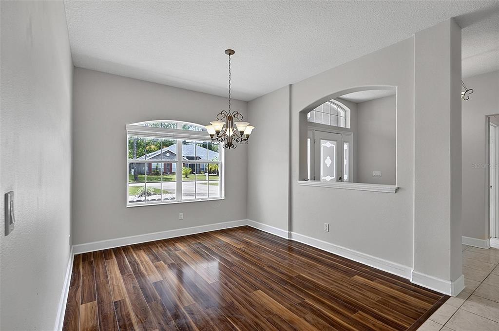 A dining room features wood-look flooring, a chandelier, and an arched opening to an entryway — 66 RAMBLEWOOD DRIVE, PALM COAST, FL