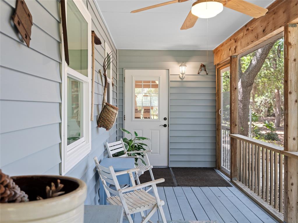 A covered porch features light blue siding, white chairs, a ceiling fan, and wooden railings — 255 MOCKINGBIRD LANE, MERRITT ISLAND, FL