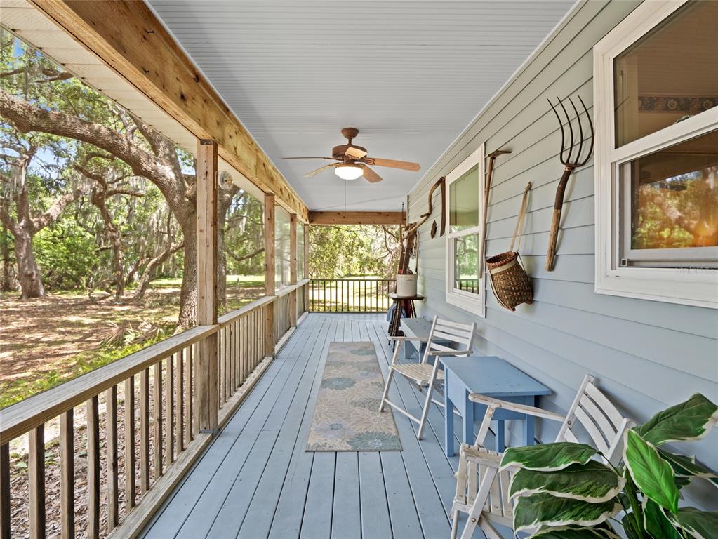 A covered porch features light blue painted wood flooring, a ceiling fan, and rustic wall decor — 255 MOCKINGBIRD LANE, MERRITT ISLAND, FL