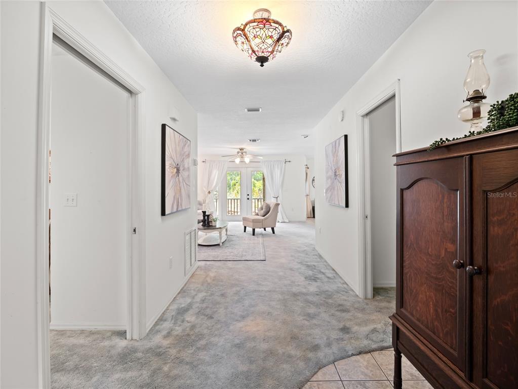 A carpeted hallway leads to a living area with glass doors and a ceiling fan — 255 MOCKINGBIRD LANE, MERRITT ISLAND, FL