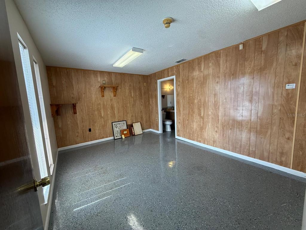 A room with wood-paneled walls, a gray speckled floor, and a doorway leading to a bathroom — 11640 ZIMMERMAN ROAD, PORT RICHEY, FL