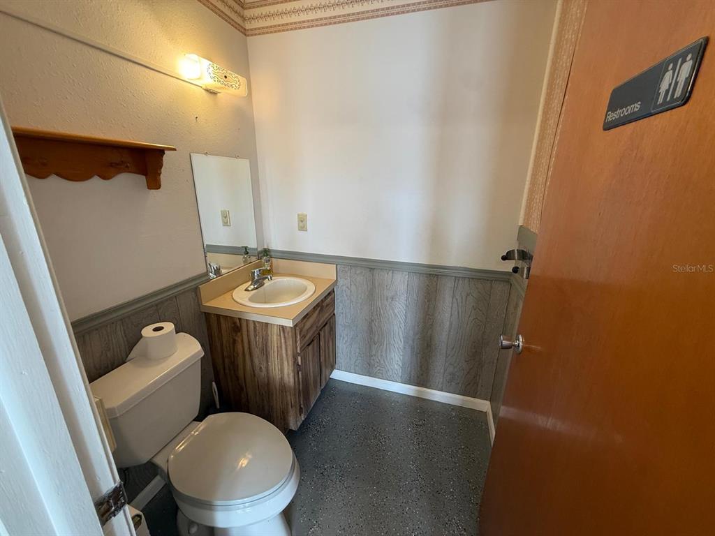 A small bathroom features a toilet, a vanity with a sink, and wood-paneled wainscoting — 11640 ZIMMERMAN ROAD, PORT RICHEY, FL