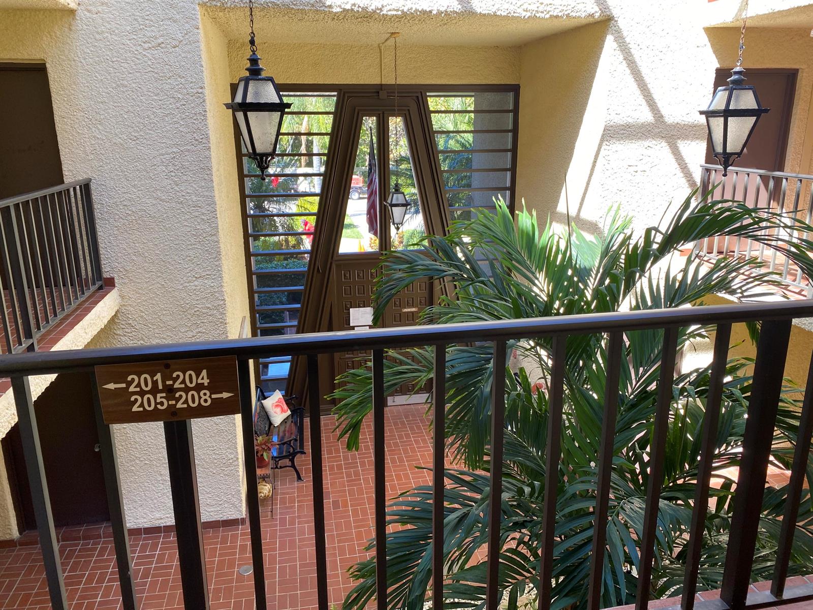 An outdoor walkway overlooks a tiled courtyard with a large palm tree and decorative lanterns — 1800 SE Saint Lucie Boulevard # 203, Stuart FL 34996, STUART, FL