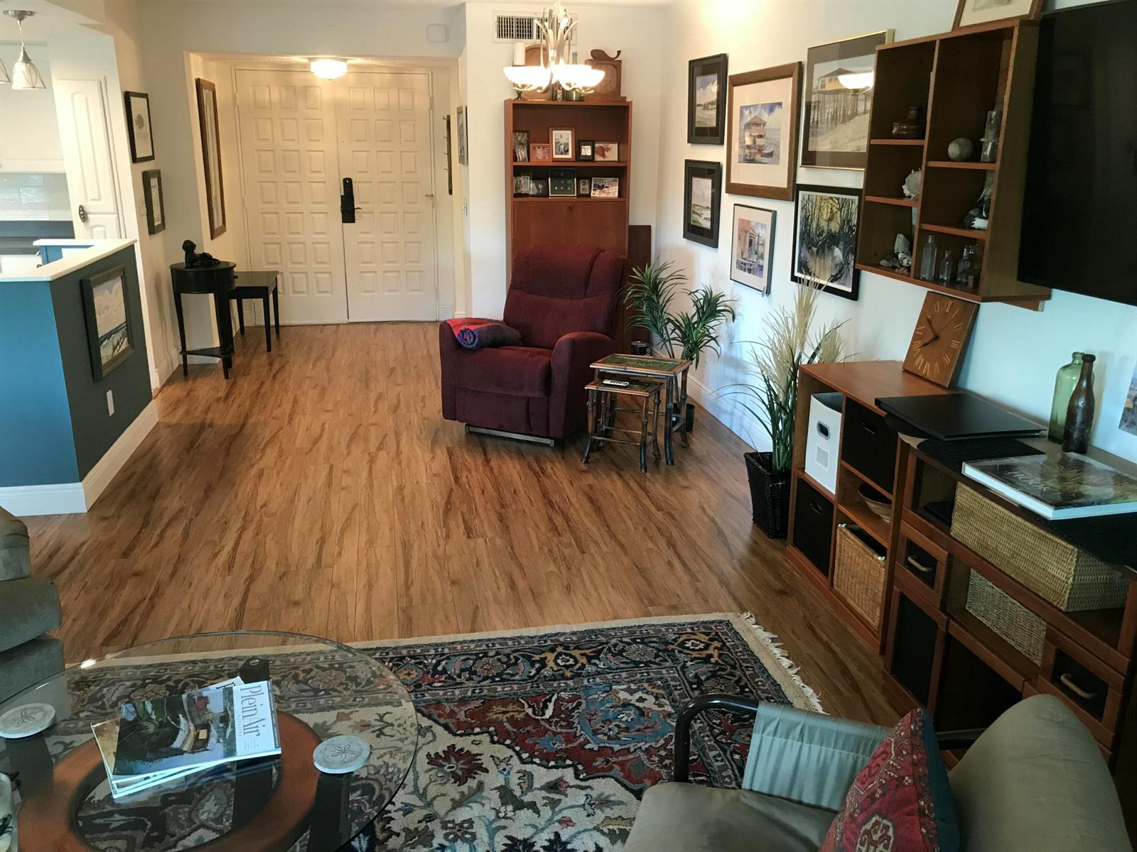 A living room features wood-look flooring, a patterned area rug, a maroon recliner, and wall art — 1800 SE Saint Lucie Boulevard # 203, Stuart FL 34996, STUART, FL