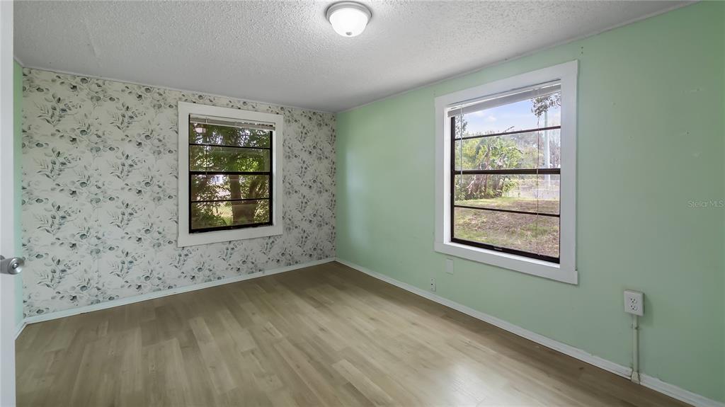 A bedroom with light green walls, a floral accent wall, and light wood-look flooring — 2201 DOLARWAY STREET, SANFORD, FL
