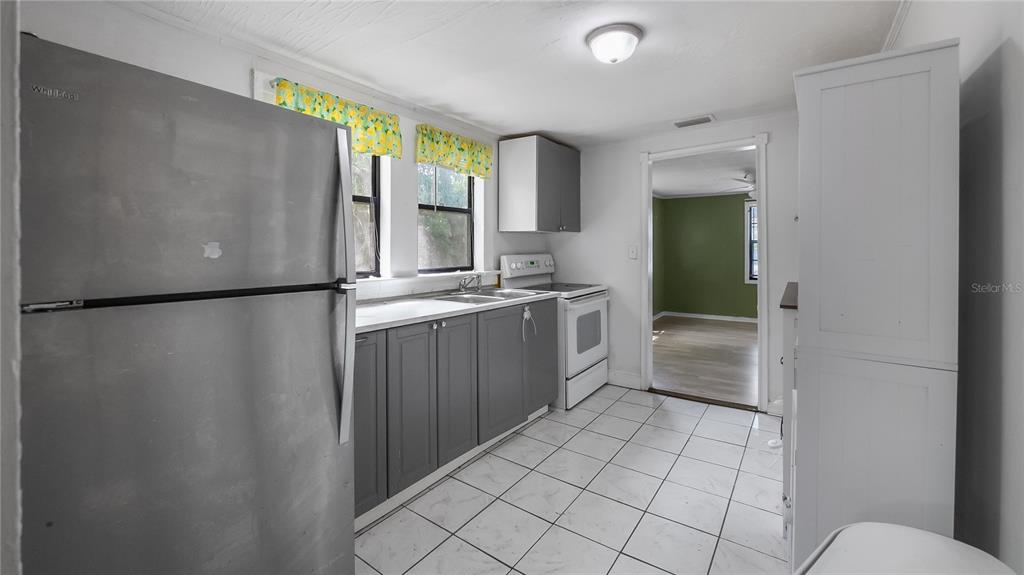 A kitchen features gray cabinets, stainless steel appliances, white tile flooring, and yellow valance curtains — 2201 DOLARWAY STREET, SANFORD, FL