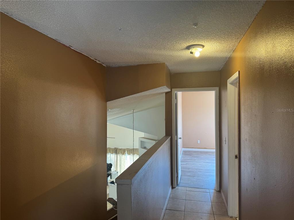 A hallway with tan walls, tile flooring, and a view overlooking a lower living area — 2231 BLUE SAPPHIRE CIRCLE, ORLANDO, FL