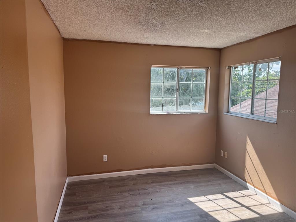 An empty bedroom with tan walls, gray wood-look flooring, and two windows — 2231 BLUE SAPPHIRE CIRCLE, ORLANDO, FL