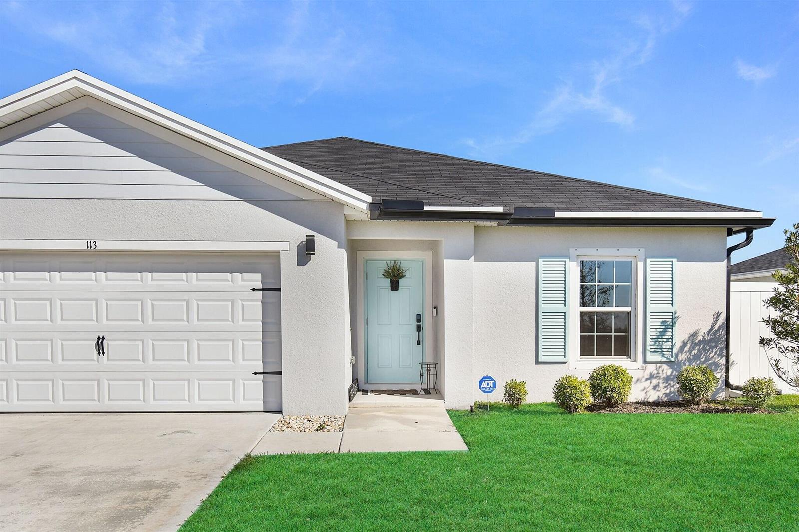 A single-story house exterior features a white stucco facade, light blue door, and garage — 113 Dabou Loop, Belle Glade FL 33430, BELLE GLADE, FL