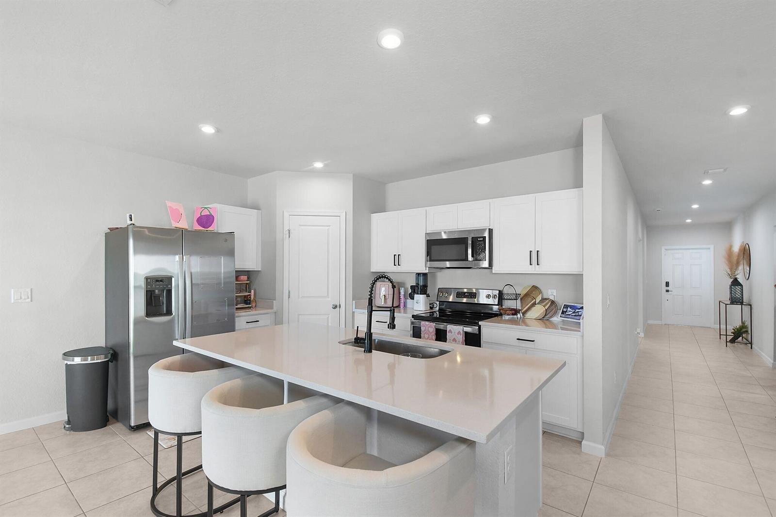 A modern kitchen features white cabinetry, stainless steel appliances, and a central island with seating — 113 Dabou Loop, Belle Glade FL 33430, BELLE GLADE, FL