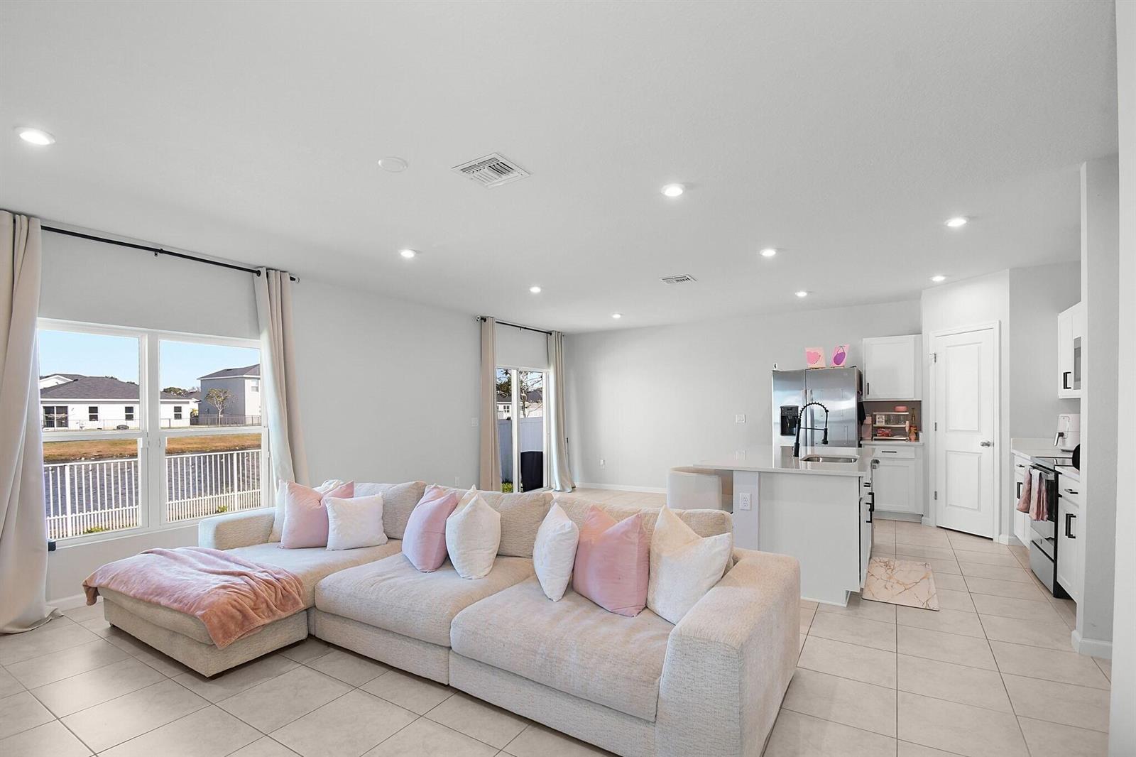A bright open-concept living room and kitchen featuring a large sectional sofa and tile flooring — 113 Dabou Loop, Belle Glade FL 33430, BELLE GLADE, FL
