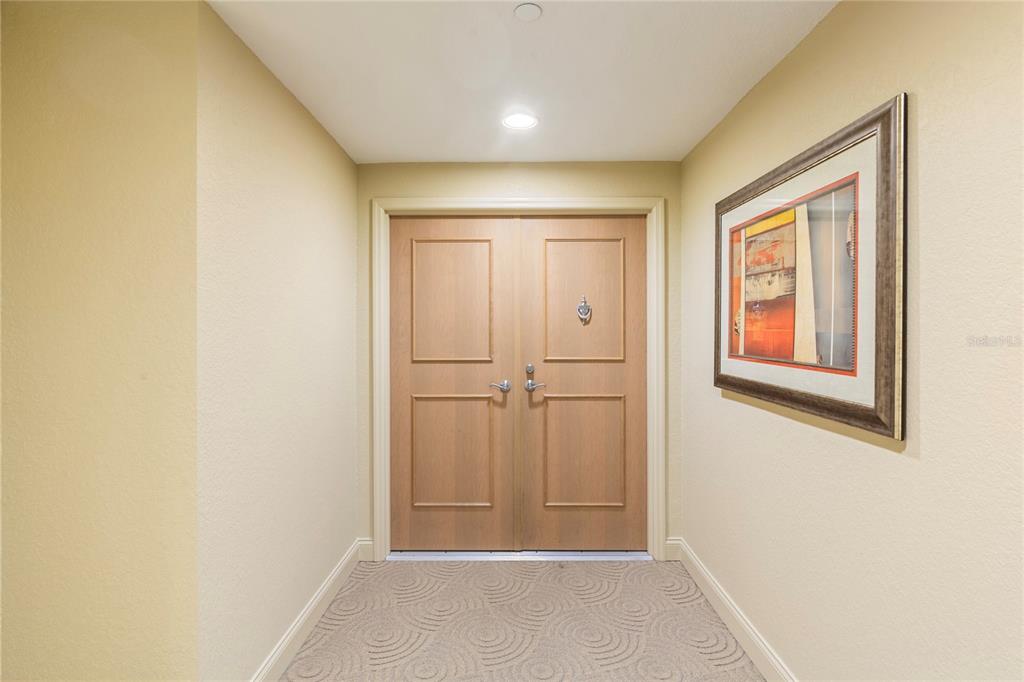 A small entryway features double wooden doors, beige walls, and patterned carpet flooring — 1200 GULF BOULEVARD UNIT 1002, CLEARWATER BEACH, FL