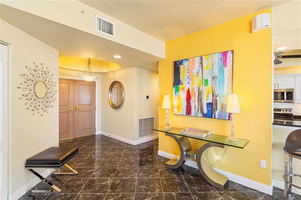 An entryway features dark marble tile flooring, a yellow accent wall, and a glass console table — 1200 GULF BOULEVARD UNIT 1002, CLEARWATER BEACH, FL