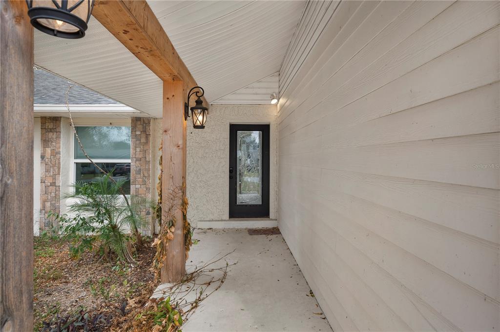 A covered entryway features a black front door, wood support beams, and light-colored siding — 132 ALACHUA DRIVE, WINTER HAVEN, FL