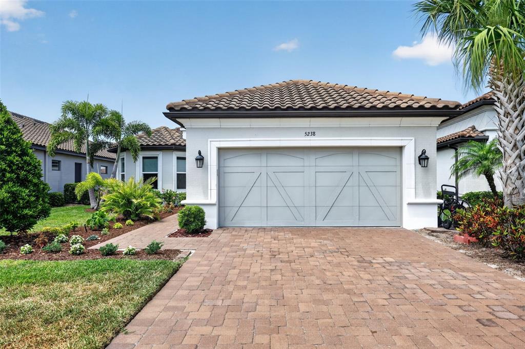 A single-story house exterior features a two-car garage, a paver driveway, and tropical landscaping — 5238 MOREY FARMS LOOP, PALMETTO, FL