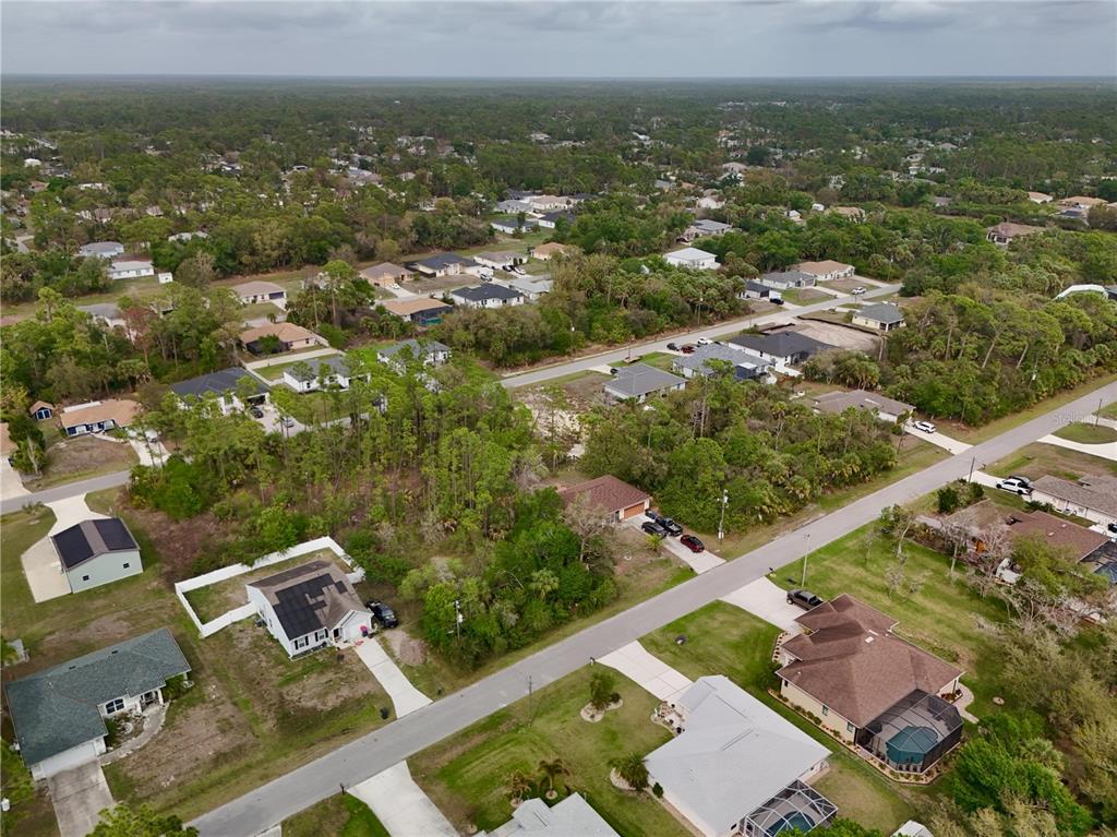 An aerial view shows a residential neighborhood with houses, driveways, and surrounding wooded areas — LA ROSA AVENUE, NORTH PORT, FL