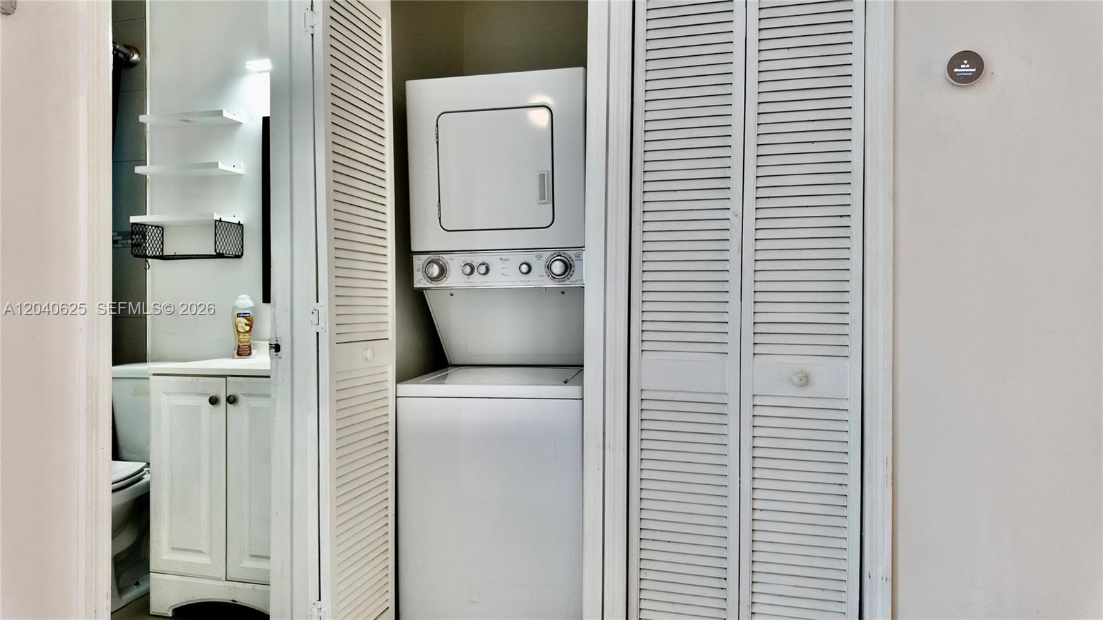 A laundry closet with a stacked washer and dryer sits beside a bathroom vanity — 822 Lenox Ave # 5, Miami Beach FL 33139, MIAMI BEACH, FL