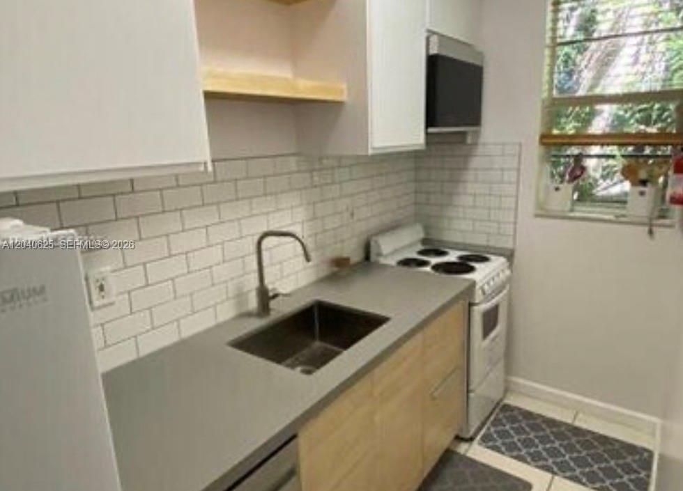 A small kitchen features light wood cabinets, gray countertops, white subway tile, and a stove — 822 Lenox Ave # 5, Miami Beach FL 33139, MIAMI BEACH, FL