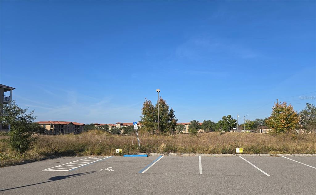 A paved parking lot sits in front of an overgrown vacant lot under a clear sky — 811 RETREAT BOULEVARD UNIT 201, DAVENPORT, FL