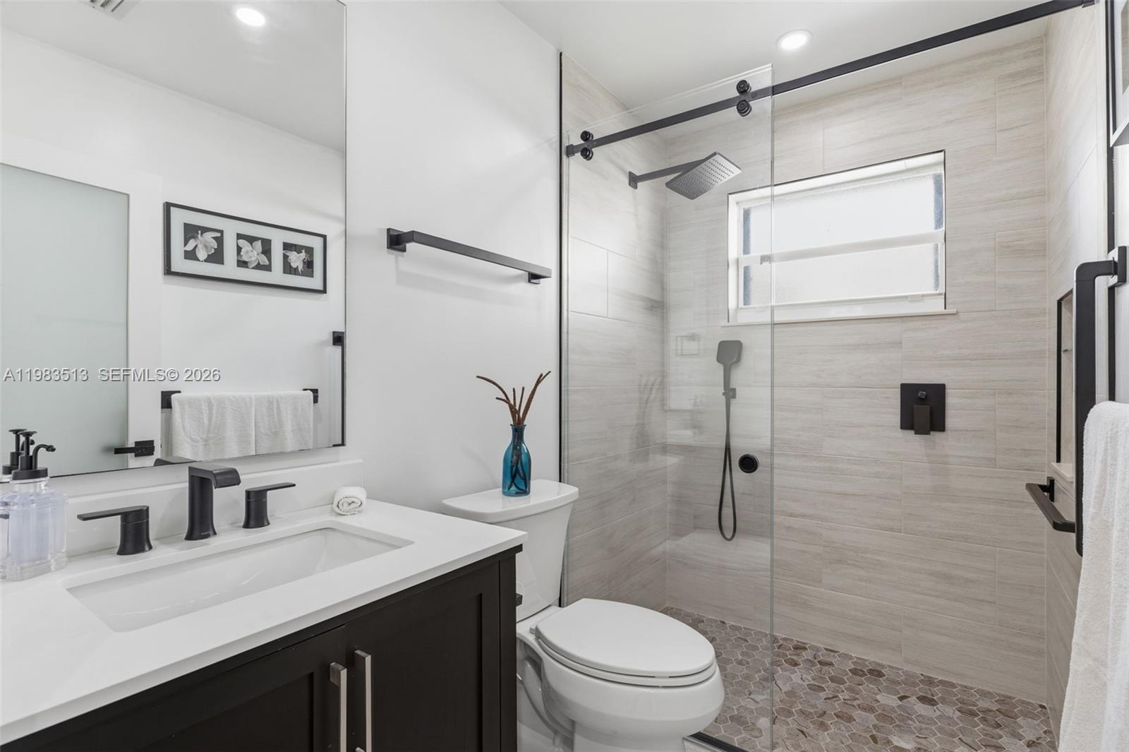 A modern bathroom features a dark vanity, a glass-enclosed shower, and light-toned tile flooring — 2485 NE 214th St, Miami FL 33180, MIAMI, FL