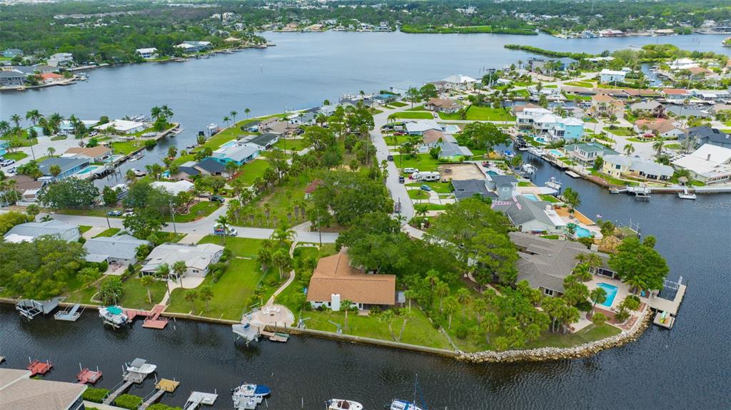 An aerial view shows waterfront homes with docks, swimming pools, and lush landscaping along canals — 8143 CHANNEL DRIVE, PORT RICHEY, FL