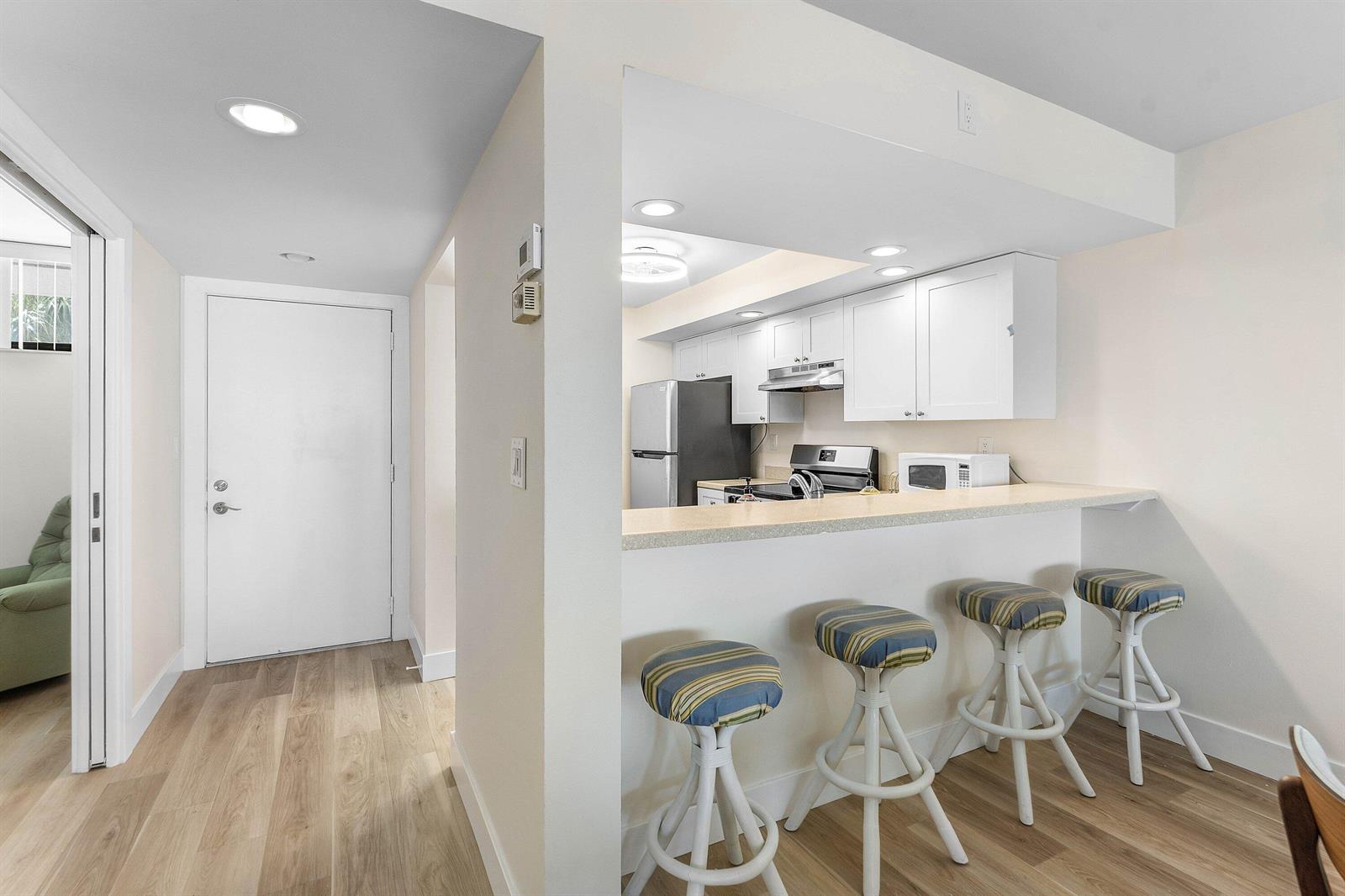 A kitchen with white cabinets and a breakfast bar with four stools faces a hallway — 1950 SW Palm City Road # 14203, Stuart FL 34994, STUART, FL
