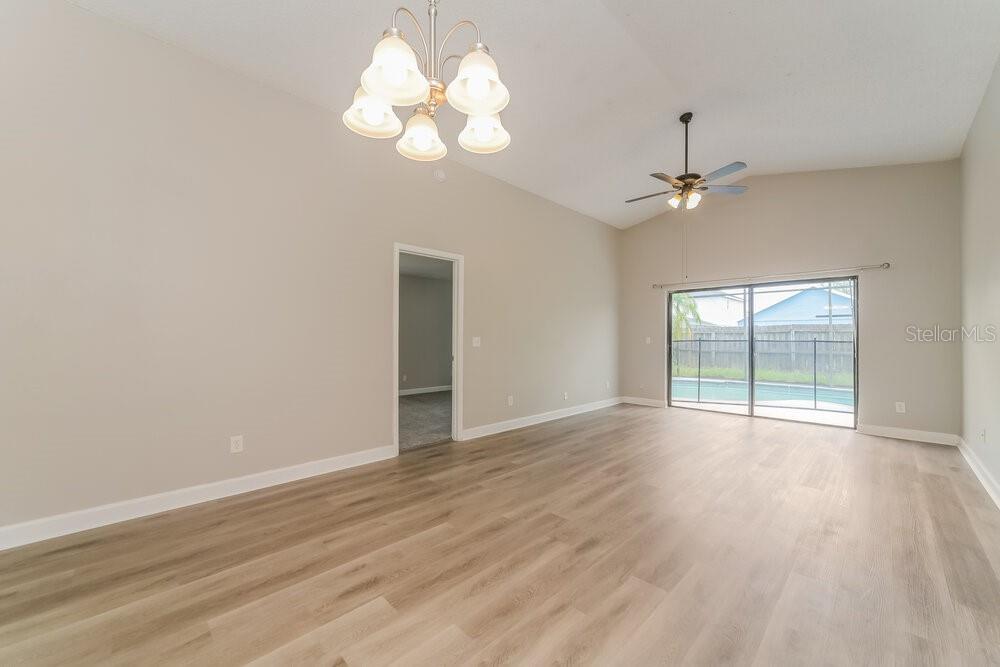 A living room with light wood-look flooring, a vaulted ceiling, a chandelier, and sliding glass doors — 13230 BOULDER WOODS CIRCLE, ORLANDO, FL