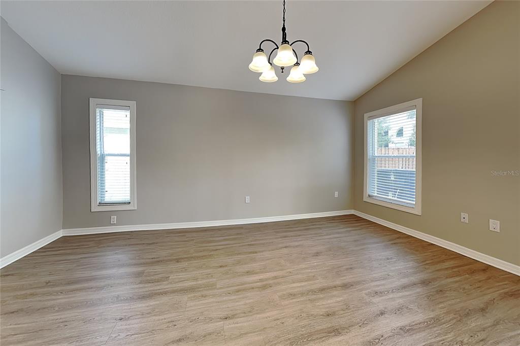 An empty room features light wood-look flooring, gray walls, two windows, and a hanging chandelier — 2517 CLARESIDE DRIVE, VALRICO, FL