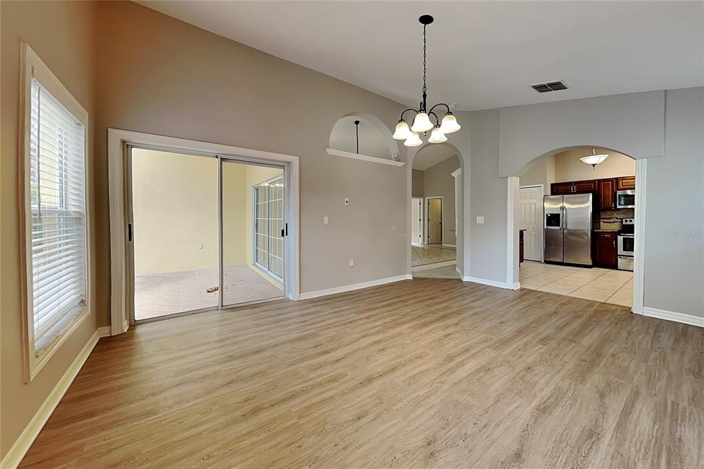An open living area features light wood-look flooring, a chandelier, and a view into the kitchen — 2517 CLARESIDE DRIVE, VALRICO, FL