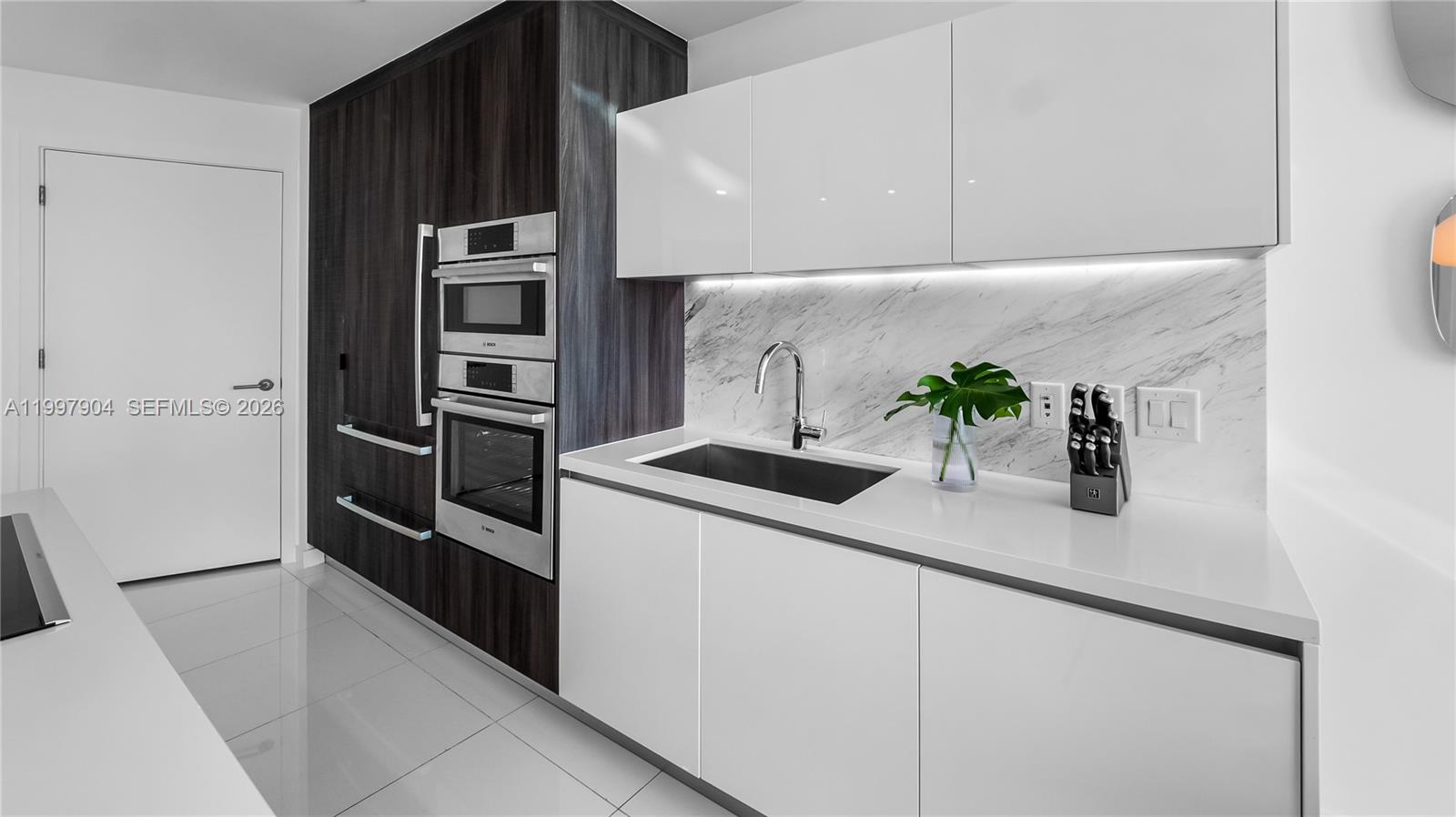 A modern kitchen features white cabinets, marble backsplash, stainless steel appliances, and dark wood paneling — 851 NE 1st Ave # 1606, Miami FL 33132, MIAMI, FL
