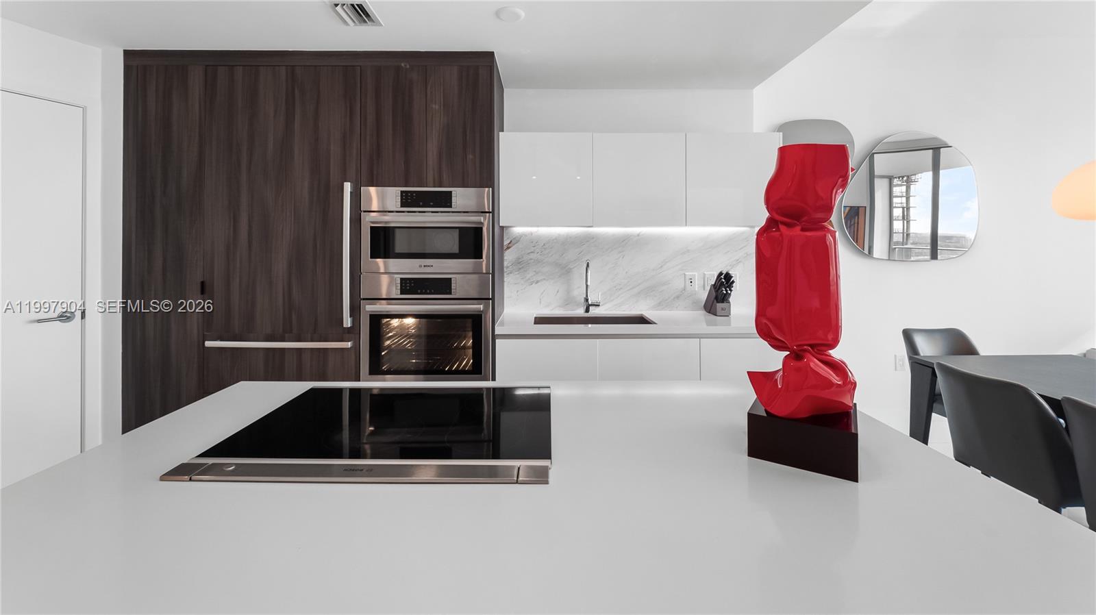 A modern kitchen features white countertops, dark wood cabinetry, stainless steel appliances, and a red sculpture — 851 NE 1st Ave # 1606, Miami FL 33132, MIAMI, FL