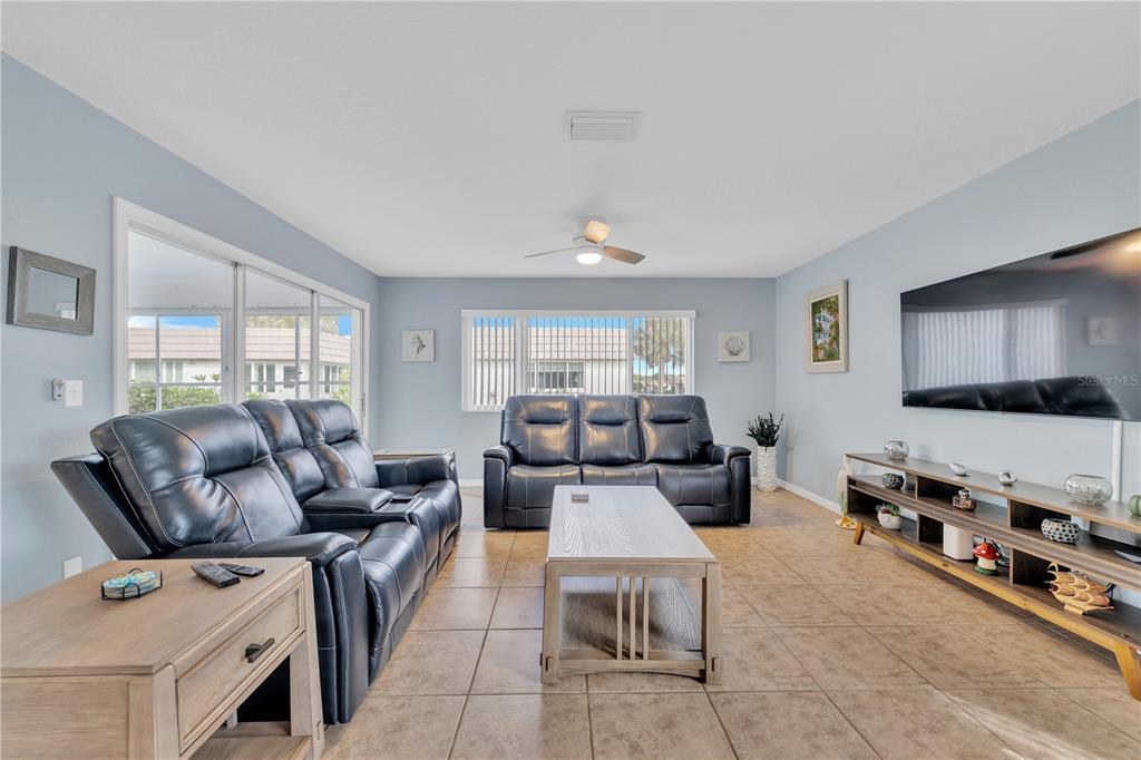A living room features light blue walls, tile flooring, two dark leather sofas, and a television — 2401 RIVERBLUFF PARKWAY UNIT V240, SARASOTA, FL