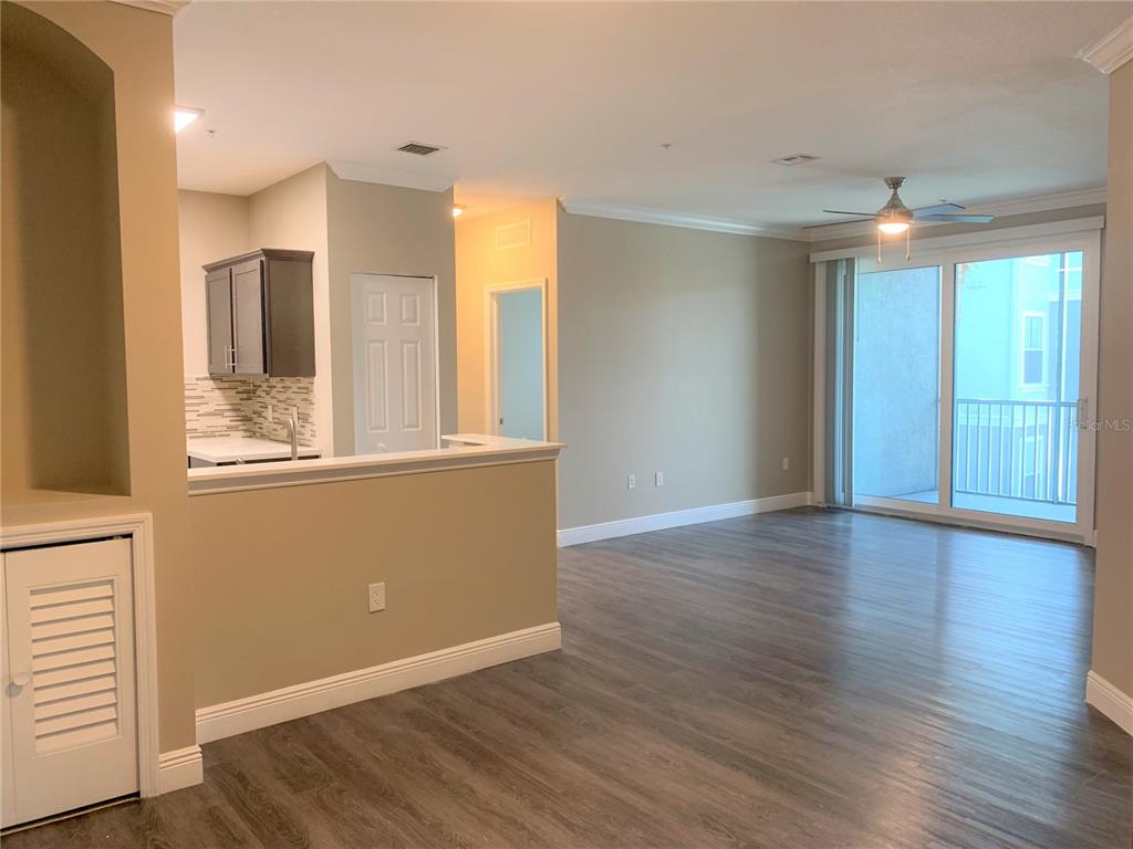 An open-concept living area features wood-look flooring, a kitchen with dark cabinets, and a balcony — 5617 LEGACY CRESCENT PLACE UNIT 201, RIVERVIEW, FL