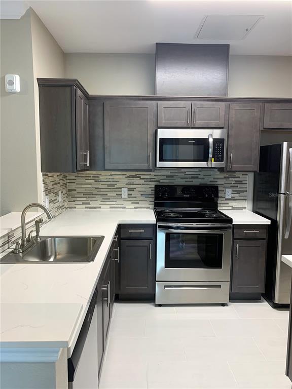 A kitchen features dark gray cabinets, stainless steel appliances, white countertops, and a tiled backsplash — 5617 LEGACY CRESCENT PLACE UNIT 201, RIVERVIEW, FL