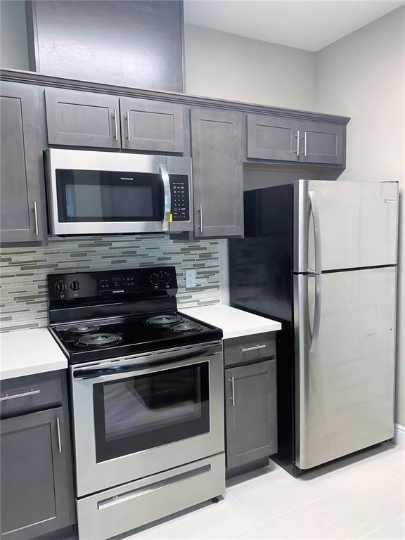 A kitchen features dark gray cabinets, stainless steel appliances, and a light-colored tiled backsplash — 5617 LEGACY CRESCENT PLACE UNIT 201, RIVERVIEW, FL