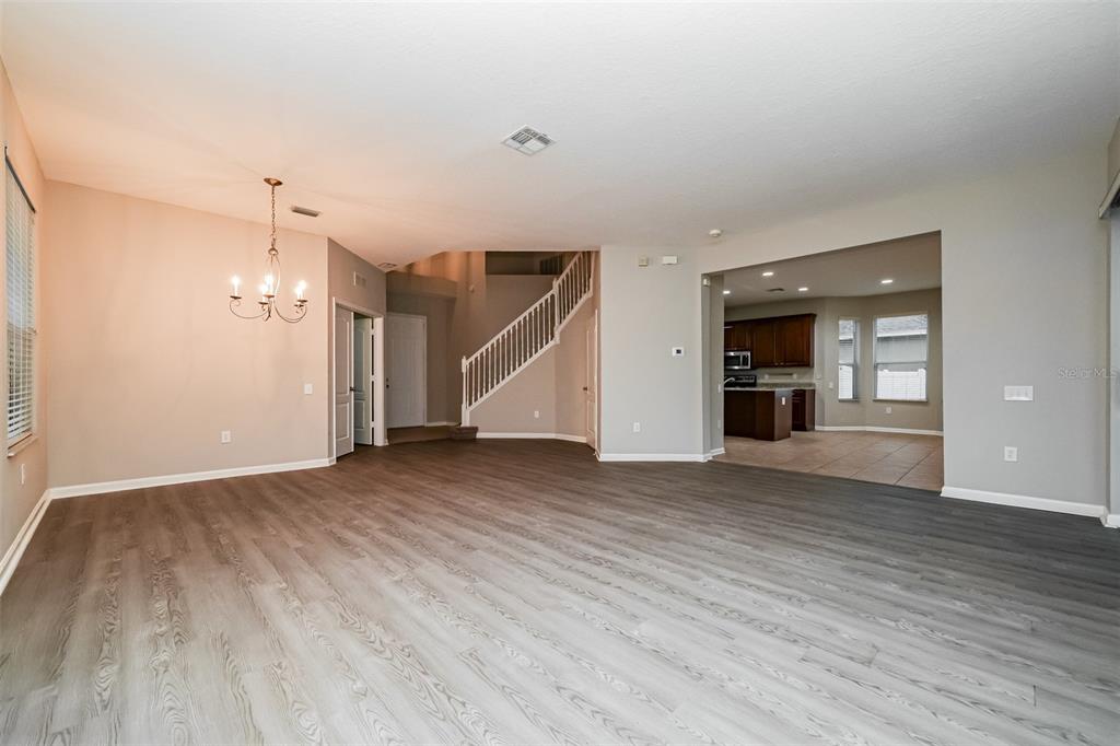 A spacious living area with gray wood-look flooring, a chandelier, and an open kitchen view — 2026 HEARTLAND CIRCLE, VALRICO, FL