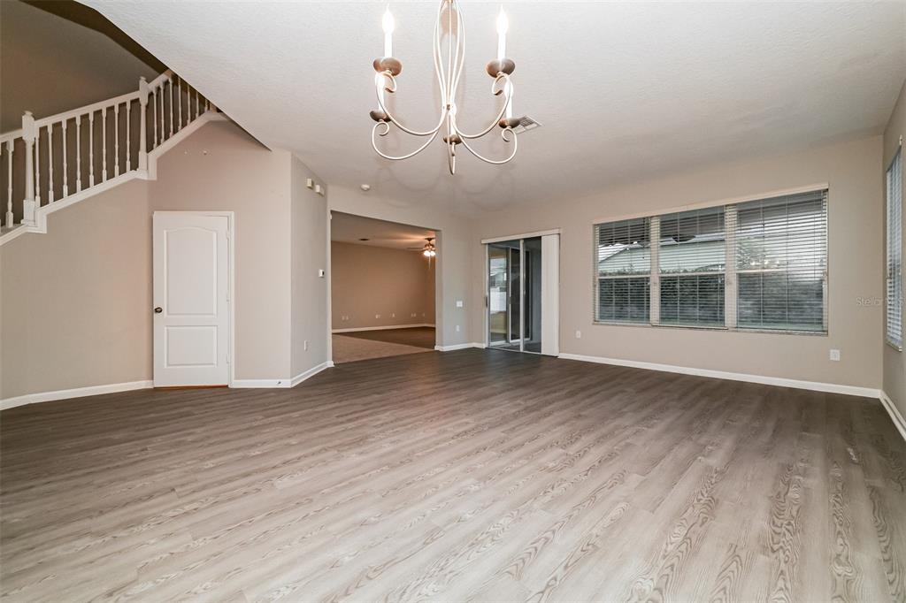An empty living room features light wood-look flooring, a chandelier, and a staircase — 2026 HEARTLAND CIRCLE, VALRICO, FL