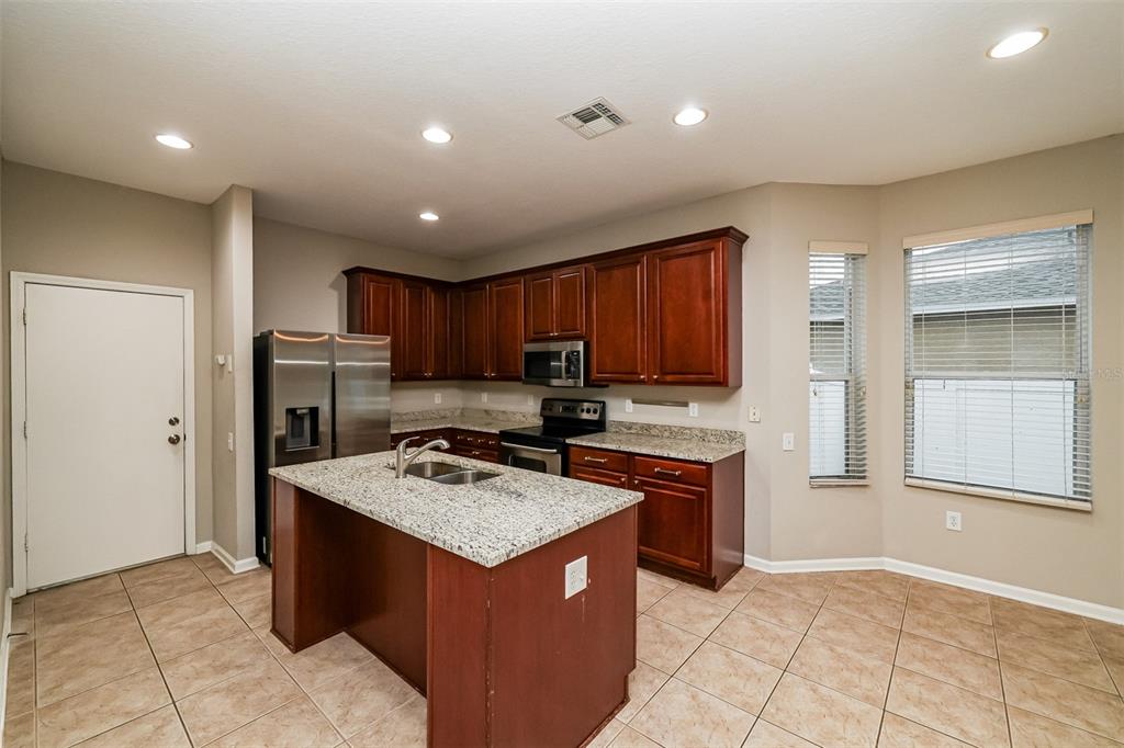 A kitchen features dark wood cabinets, granite countertops, a center island, and stainless steel appliances — 2026 HEARTLAND CIRCLE, VALRICO, FL