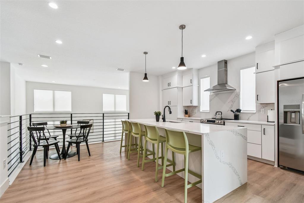 A modern kitchen features a white quartz island with green stools and stainless steel appliances — 3840 POMPANO DRIVE SE, ST PETERSBURG, FL