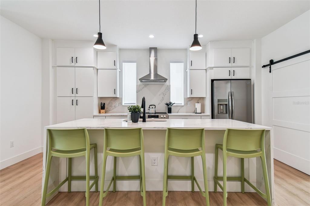 A modern kitchen features white cabinetry, a marble-topped island, and four lime green bar stools — 3840 POMPANO DRIVE SE, ST PETERSBURG, FL