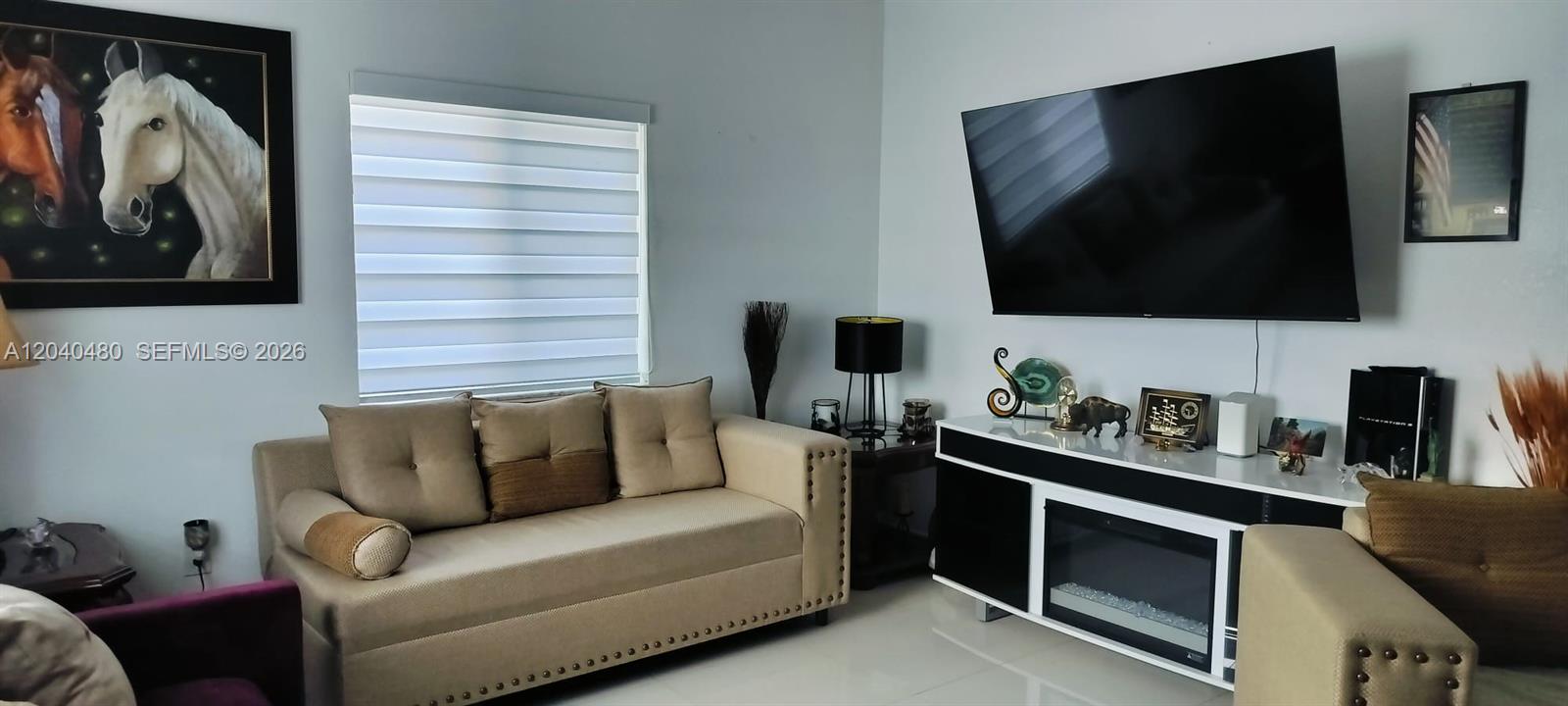 A living room features a beige sofa, a television mounted above a fireplace console, and horse artwork — 4223 NW 32nd Ave, Miami FL 33142, MIAMI, FL