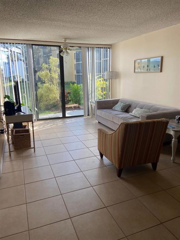 A living room with tile flooring, a beige sofa, a striped armchair, and sliding glass doors — 2424 W TAMPA BAY BOULEVARD UNIT L105, TAMPA, FL