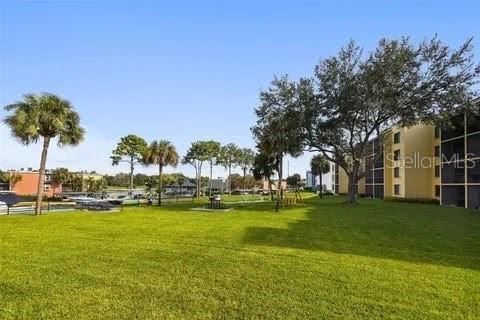 A grassy lawn extends toward a multi-story apartment building and trees under a clear sky — 2424 W TAMPA BAY BOULEVARD UNIT L105, TAMPA, FL