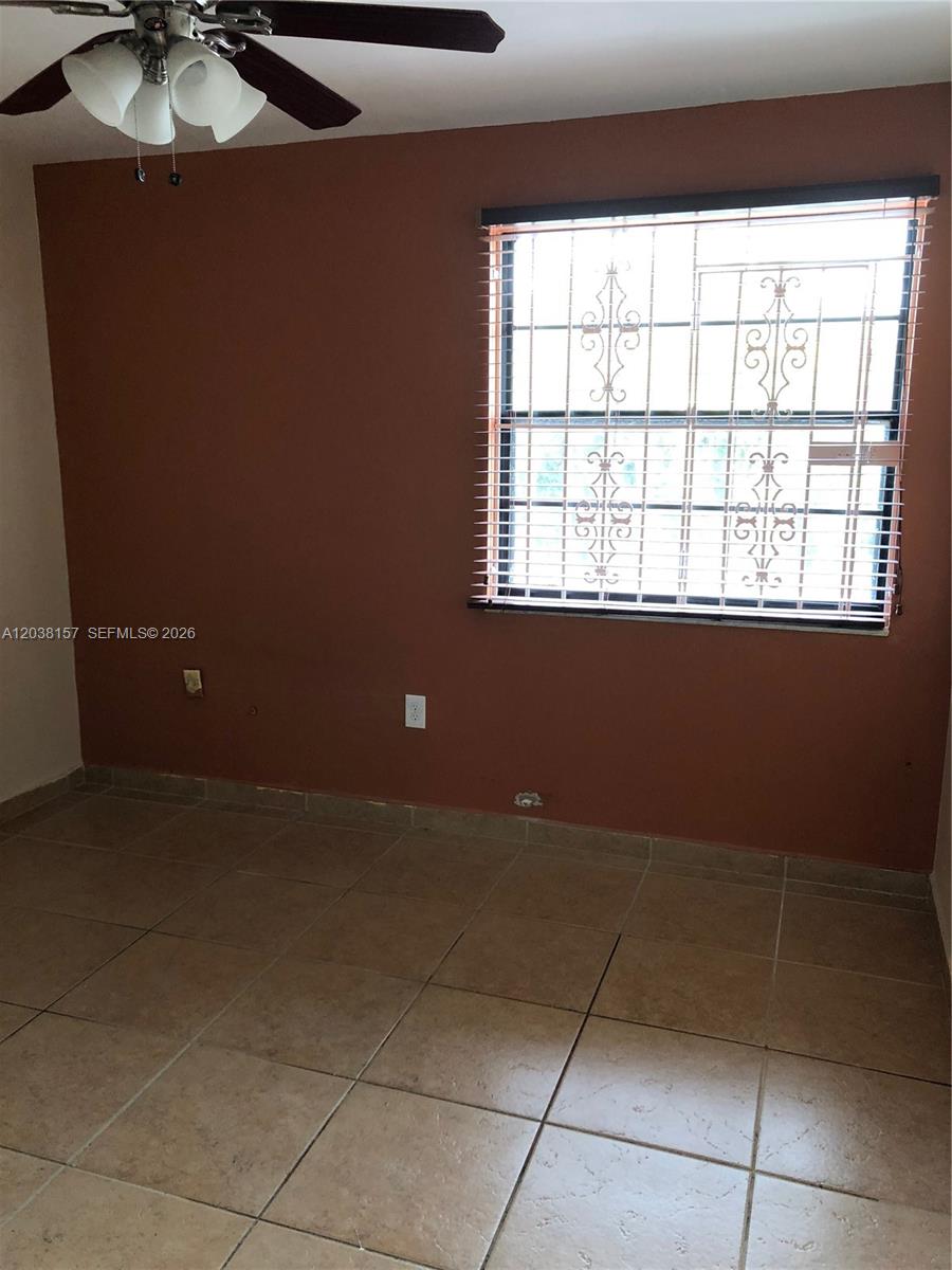 An empty room features terracotta-colored walls, tiled flooring, a ceiling fan, and a barred window — 3808 SW 79th Ave # 63, Miami FL 33155, MIAMI, FL